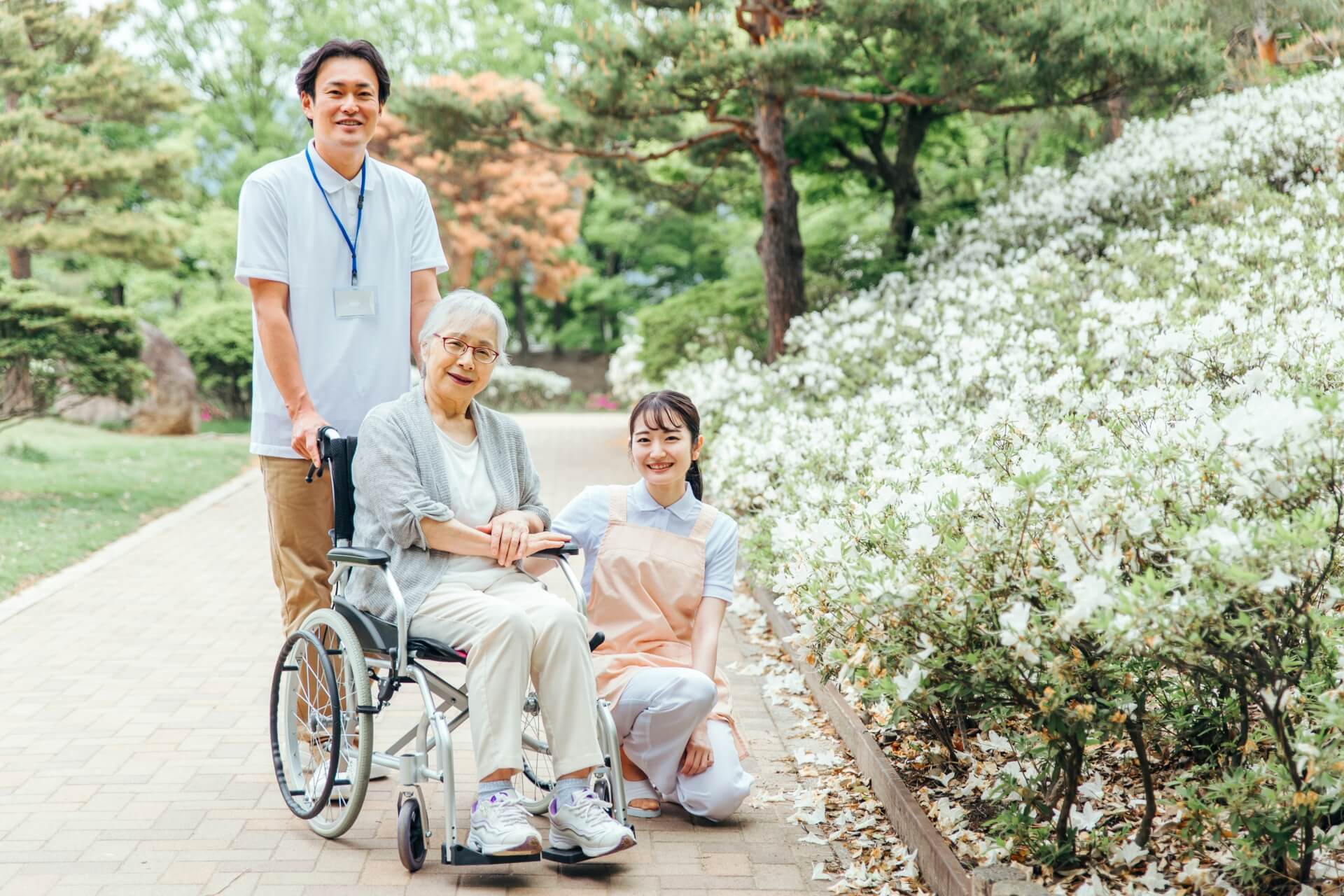 車いすに座る老女と介助する男性介護職員。その片割れで膝をつき微笑む女性介護職員