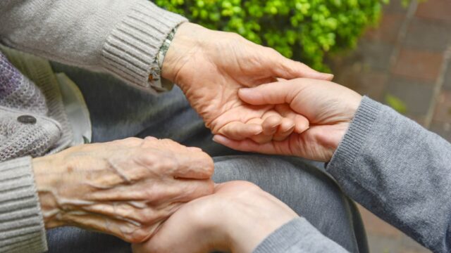 高齢者と若い方が両手を握っている。